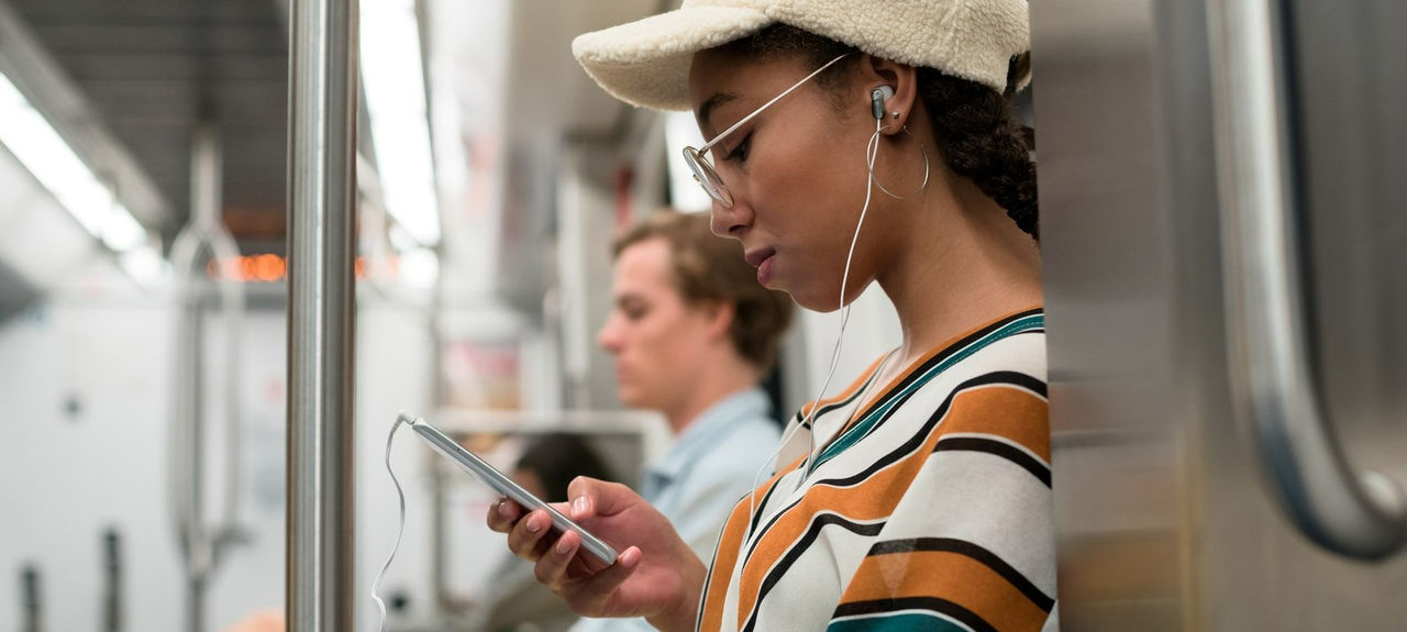 Multiracial teenager listening to music with earphones and looking at her phone while traveling on the subway.